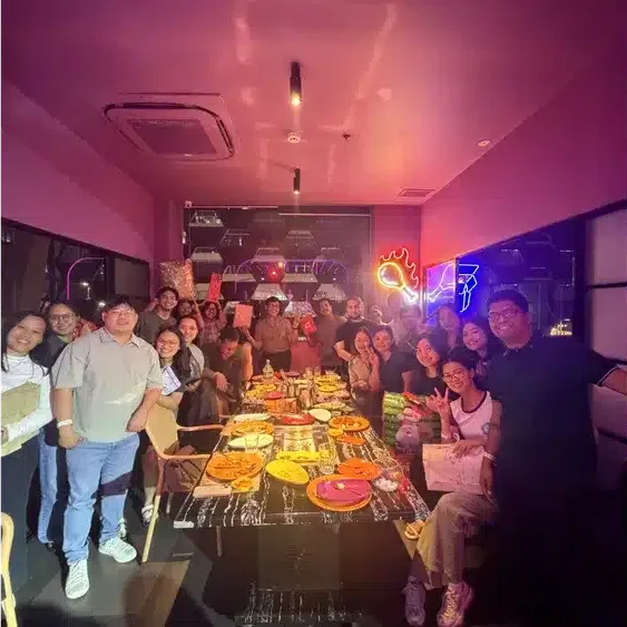 Diverse group of friends and family posing for a photo around a table full of food at a vibrant restaurant.