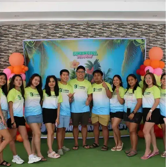 A diverse group of people in matching t-shirts pose for a photo in front of a celebratory banner.