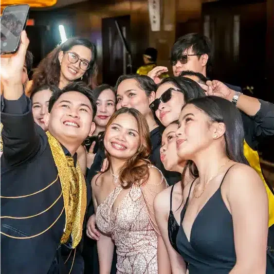 A group of friends taking a selfie at a formal gathering, smiling and posing for the camera.