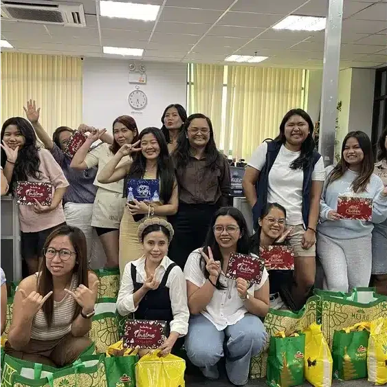 A diverse group of women in an office environment, posing for a photo with Christmas gifts and smiles, some holding festive c